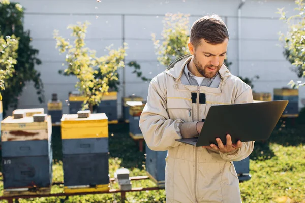 男农学家或穿着防护服在养蜂场笔记本电脑上工作的工程师 — 图库照片