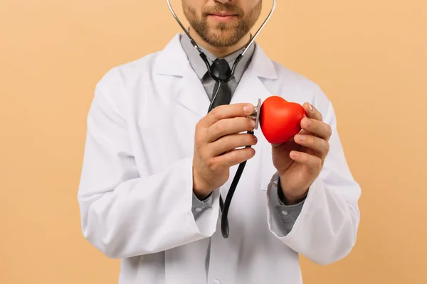 男性医師心臓病は ベージュの背景に聴診器で心臓に耳を傾けます — ストック写真