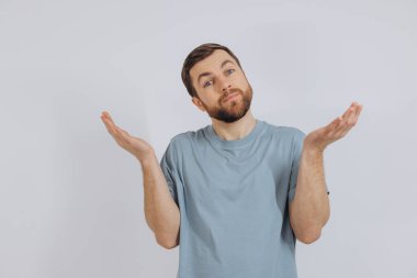 Mavi tişörtlü, modern sakallı orta yaşlı bir adamın portresi, beyaz arka plandaki duyguları bilmediğini gösteriyor.