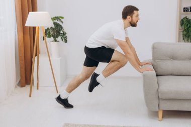 Pozitif atletik sakallı orta yaşlı bir adam evde esniyor, dizüstü bilgisayar kullanıyor, internette spor videoları izliyor, fitness dersi alıyor, kopya çekiyor. Sağlıklı yaşam tarzı, kendini soyutlama sporu.