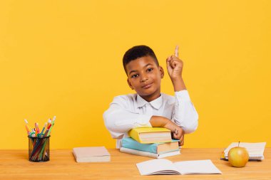 Mutlu Afrikalı okul çocuğu ders sırasında masada oturuyor ve kolunu kaldırıyor. Okul konseptine dönelim..