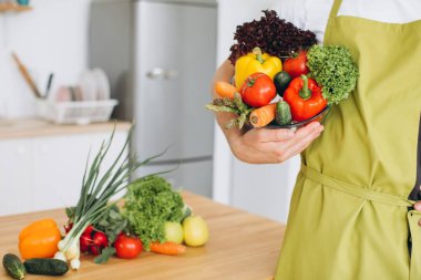 Mutfağın arka planında taze sebze tabağı ve çeşitli sebzelerle dolu mutfak masası tutan bir adam..