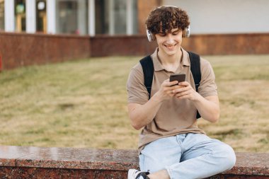 Çekici kıvırcık erkek üniversitesi ya da kampüste telefonla dolaşan üniversite öğrencisi.