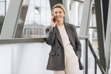 Takım elbiseli, gri ceketli, güzel bir iş kadınının portresi modern şehir arka planında gülümseyen ve konuşan.