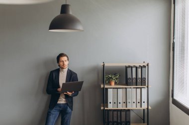 Modern ofiste takım elbiseli ve dizüstü bilgisayar kullanan genç ve neşeli iş adamının görüntüsü