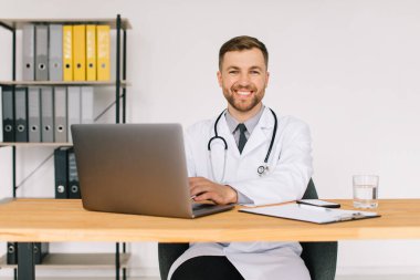 Mutlu erkek doktor iş yerinde dizüstü bilgisayarla otururken internetteki tıbbi web sitesini ya da eğitim seminerini izliyor..