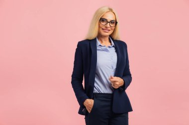 Pembe arka planda orta yaşlı çekici bir iş kadınının portresi.