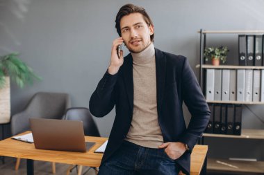 Takım elbiseli yakışıklı iş adamı modern ofiste telefonla konuşuyor.