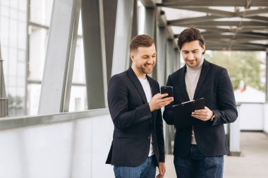 İki modern iş adamı bir şeyi tartışıyor ve birbirlerine akıllı telefondan kentsel ofis ve binaların arka planına karşı çıkıyorlar.