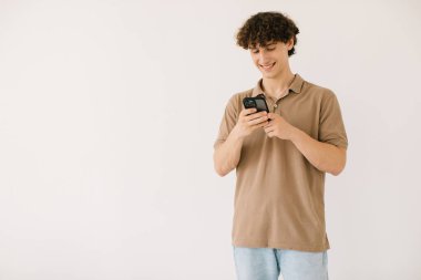 Çekici genç bir erkek öğrenci telefonu beyaz bir arkaplanda kullanıyor.