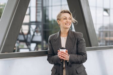 Olgun bir iş kadınının portresi. Duygularıyla gülümseyen ve modern şehir arka planında kahve içen.
