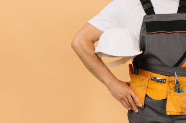 Bej arka planda kask tutan erkek inşaat işçisi.