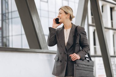 Takım elbiseli, gri ceketli, güzel bir iş kadınının portresi modern şehir arka planında gülümseyen ve konuşan.