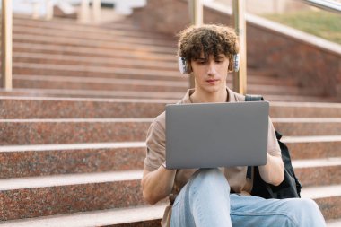 E-öğrenme, uzaktan öğrenme veya uzaktan öğrenme kavramı, üniversitede basamaklarda dizüstü bilgisayar kullanan genç kıvırcık saçlı okul çocuğu, üniversite ya da üniversite öğrencisi