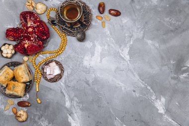 Geleneksel Arap sofra takımı ve yemek takımlarıyla süslü afiş, bir fincan çay, Kuran ve gri taşlı arka planda tespih. Ramazan masa üstü görünümü