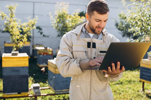 男农学家或穿着防护服在养蜂场笔记本电脑上工作的工程师 — 图库照片