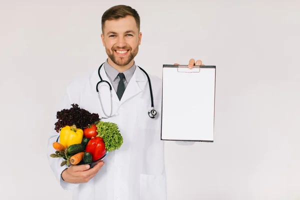 新鮮な野菜やフォルダを保持している聴診器を持つ男性医師栄養士とともにコピースペース白の背景 — ストック写真