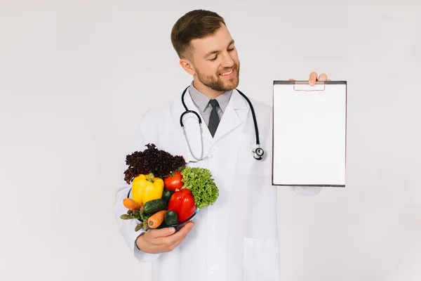 新鮮な野菜やフォルダを保持している聴診器を持つ男性医師栄養士とともにコピースペース白の背景 — ストック写真