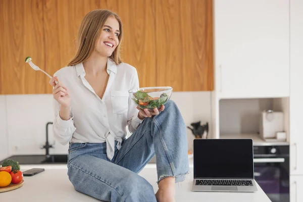 Щаслива Усміхнена Блондинка Сидить Кухонному Столі Їсть Домашній Салат Ноутбук — стокове фото