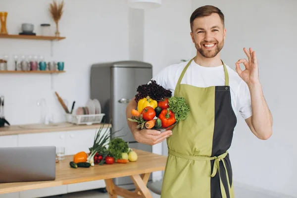 キッチンを背景に新鮮な野菜のプレートを持って幸せな男の肖像画自宅で — ストック写真