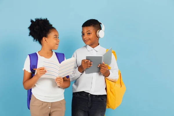 アフリカ系の男子学生とアフリカ系アメリカ人の女子学生が青を背景に学校の教室で一緒にアウトラインを読んでいます — ストック写真