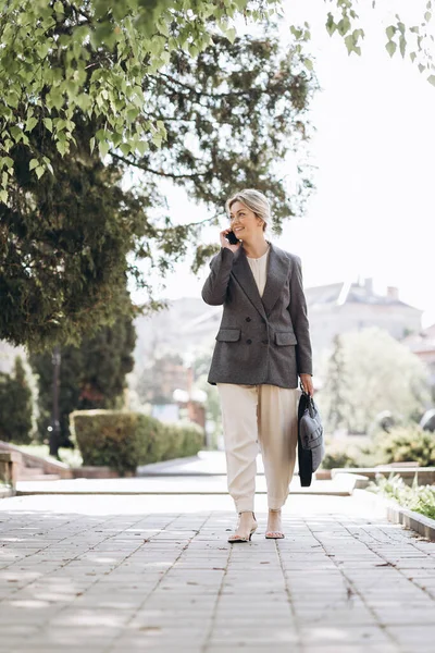 熟女ブロンドの笑顔ビジネス女性は街の通りを歩いて 電話で話す — ストック写真
