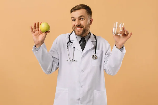 Male Nutritionist Doctor Stethoscope Smiling Holding Water Apple Beige Background — Stock Photo, Image