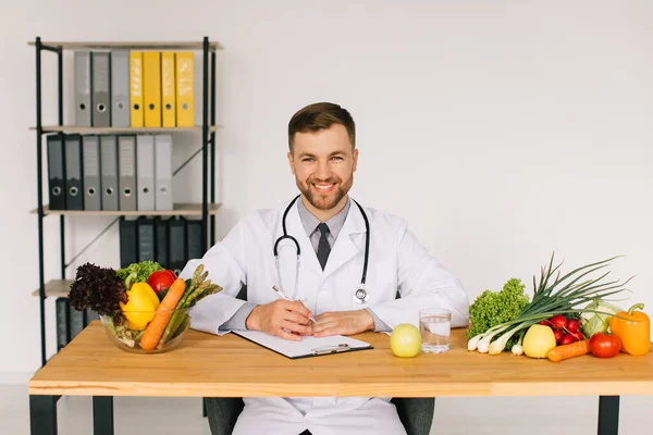 新鮮な野菜の間でオフィスのデスクで職場に座って幸せな医師栄養士 食事計画の概念 — ストック写真