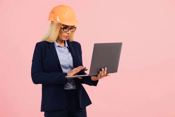 戴眼镜的建筑师或工程师女士在粉色背景上使用笔记本电脑 — 图库照片
