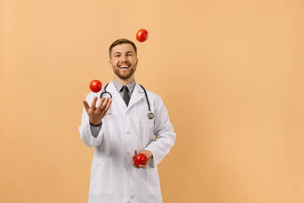 Male Nutritionist Doctor Stethoscope Smiling Juggling Tomatoes Beige Background Diet — Stock Photo, Image