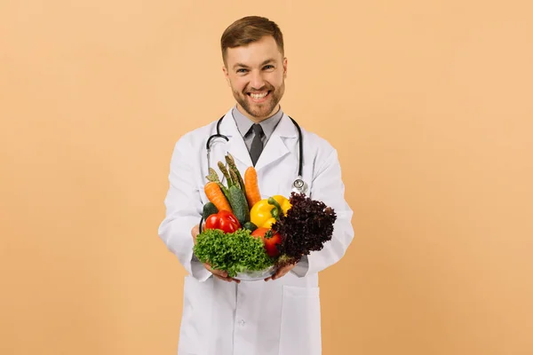 Ευτυχισμένη Διατροφολόγος Αρσενικό Γιατρό Στηθοσκόπιο Δείχνει Φρέσκα Λαχανικά Μπεζ Φόντο — Φωτογραφία Αρχείου