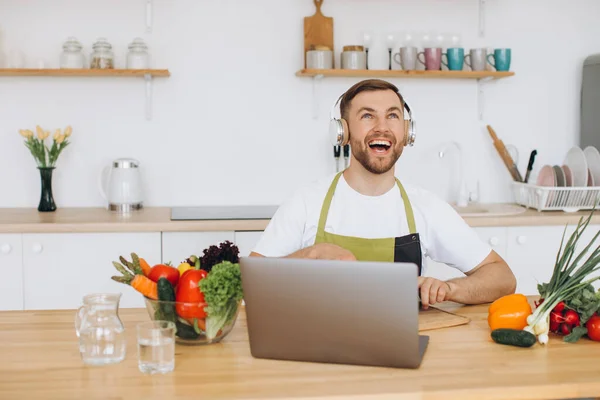 Happy Man Headphones Preparing Salad Kitchen Fresh Vegetables Looking Laptop — Stock Photo, Image