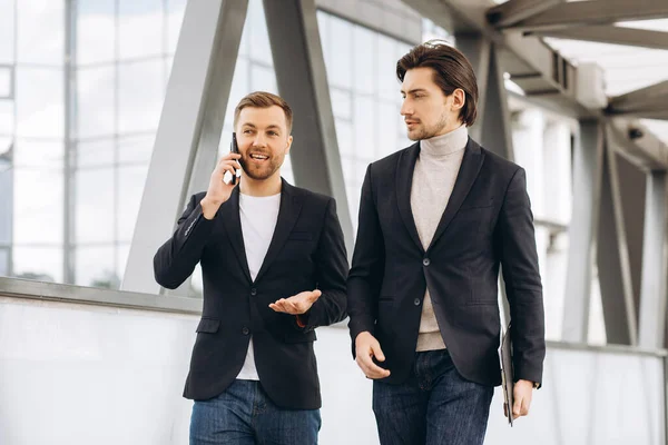 電話と書類のフォルダを持つ2人の近代的なビジネスマンが何かを議論し 都市のオフィスや建物の背景に橋を渡ります — ストック写真