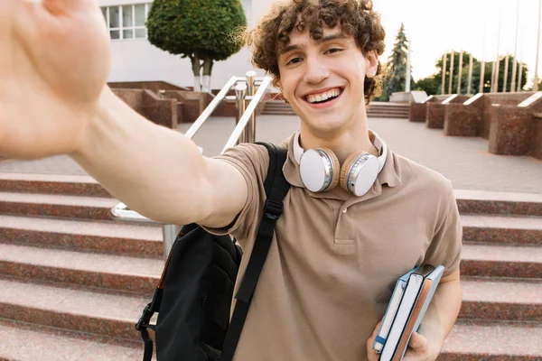 ヘッドフォンで魅力的な巻き毛の男性学生の肖像笑顔と自画撮り ビデオ通話のコンセプト — ストック写真