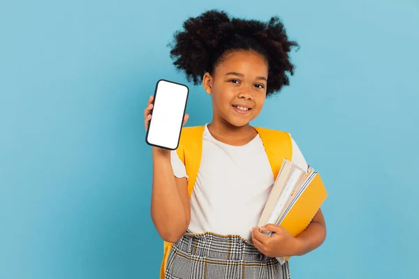 興奮した小さなアフリカ系アメリカ人の女子高生が携帯電話の空画面をブルースタジオの背景に提示で大きなセルを保持 スマートフォンディスプレイ Mockup — ストック写真