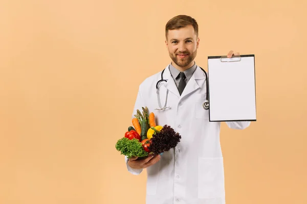 配戴听诊器的男医生营养师手持新鲜蔬菜和带有米色背景复制空间的文件夹 — 图库照片