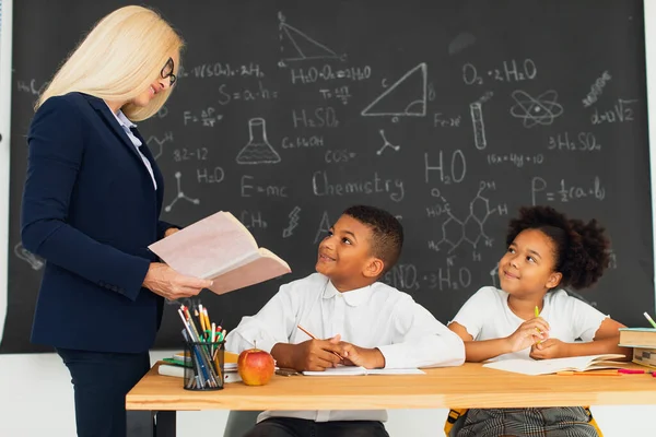 Kvinnlig Lärare Undervisar Skolbarn Som Sitter Vid Ett Skrivbord Och — Stockfoto
