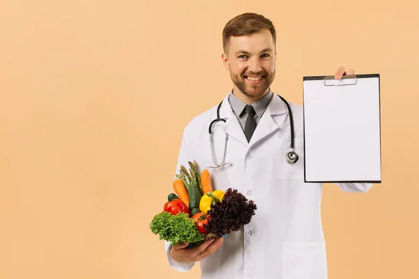 新鮮な野菜やフォルダを保持している聴診器を持つ男性医師栄養士とともにコピースペースでベージュの背景 — ストック写真