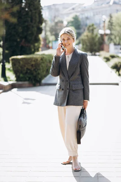 Mature blond smiling business woman walks the city streets and speaks on the phone