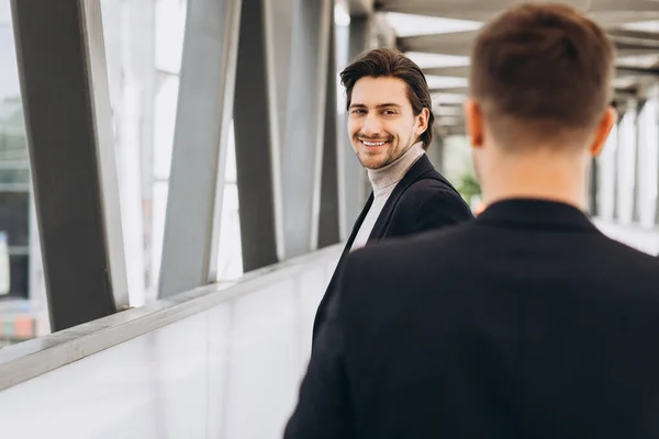 都市部のオフィスやビルを背景に二人の現代のビジネスマンが笑顔で挨拶し 何かを言う — ストック写真