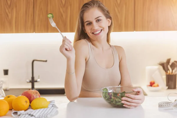 キッチンでのワークアウト後のエネルギー回復のための新鮮な野菜サラダを食べるテープを測定するスポーツウェアで幸せな魅力的な千年の女性 — ストック写真