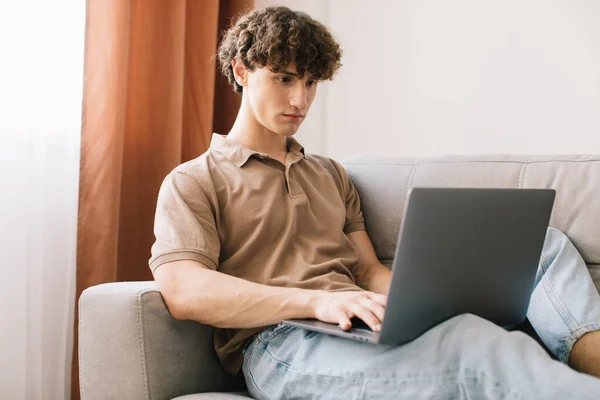 stock image Portrait of attractive young curly hair man using laptop while sitting on sofa at home