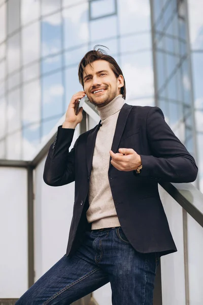 都市部の建物やオフィスの背景に電話で話をスーツでハンサムな幸せな男性ビジネスマンの肖像画 — ストック写真