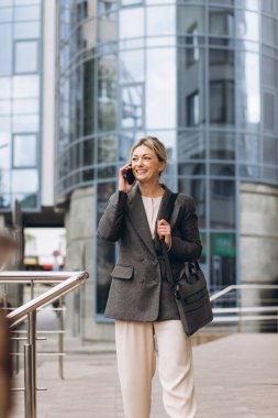 Takım elbiseli, gri ceketli, güzel bir iş kadınının portresi modern şehir arka planında gülümseyen ve konuşan.