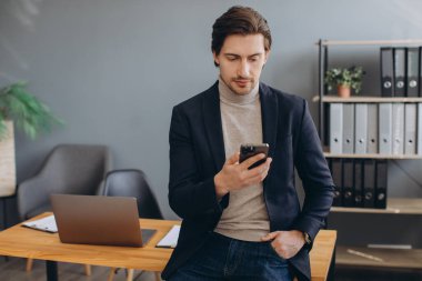 Takım elbiseli yakışıklı iş adamı modern ofiste telefonla konuşuyor.