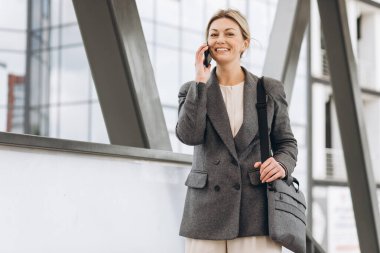 Takım elbiseli, gri ceketli, güzel bir iş kadınının portresi modern şehir arka planında gülümseyen ve konuşan.
