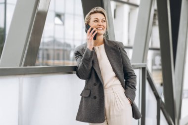 Takım elbiseli, gri ceketli, güzel bir iş kadınının portresi modern şehir arka planında gülümseyen ve konuşan.
