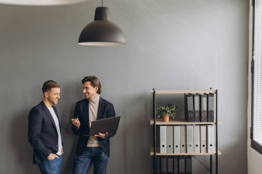 Genç iş adamları modern ofiste dizüstü bilgisayarlarını tutarak bir araya gelip...