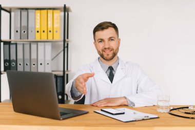 Mutlu erkek doktor iş yerinde dizüstü bilgisayarla otururken internetteki tıbbi web sitesini ya da eğitim seminerini izliyor..