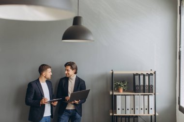 Genç iş adamları modern ofiste dizüstü bilgisayarlarını tutarak bir araya gelip...